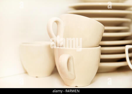 Bianco tazze di caffè con piastra di servizio impostato sul ripiano su sfondo bianco, vicino. Tazze da caffè con vassoi presso il bar. White set completo di stoviglie. Tazze, bicchieri. Foto Stock