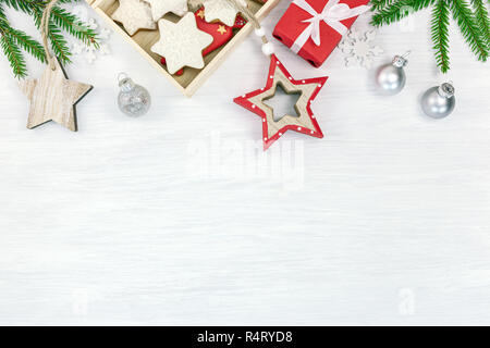 Bianco Natale vacanze con sfondo verde abete rami, box con fatti a mano biscotti di panpepato, sfere di vetro e legno stelle rosse. top view wi Foto Stock