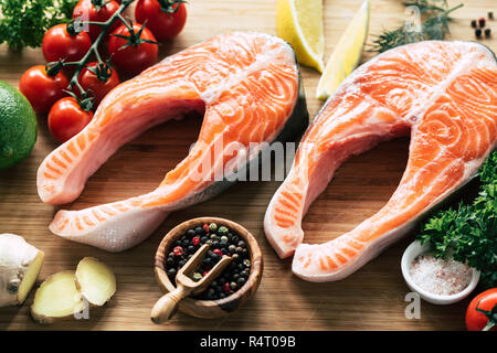 Materie filetti di salmone, spezie e verdure pronte per la cottura. Filetto di salmone su ossa, misti pepe, pomodori ciliegia, rosa sale marino, lo zenzero e limone Foto Stock
