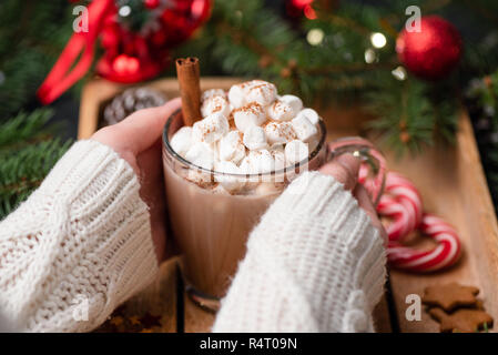 Donna mani tazza di cioccolata calda con marshmallows. Vista ingrandita, il fuoco selettivo. Festa di Natale o Capodanno bevande. Avvento, vacanze inverno Foto Stock