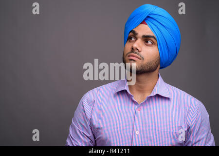 Bel giovane imprenditore indiano indossando turbante contro grigio ba Foto Stock
