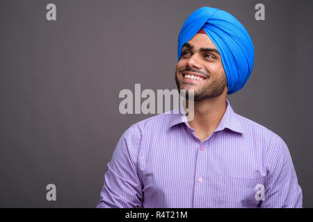 Bel giovane imprenditore indiano indossando turbante contro grigio ba Foto Stock