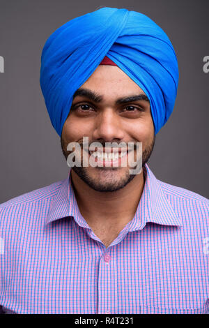 Bel giovane imprenditore indiano indossando turbante contro grigio ba Foto Stock