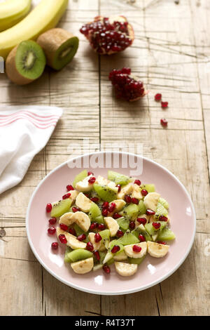 Insalata di fette di vari frutti e semi di melograno su uno sfondo di legno. Foto Stock
