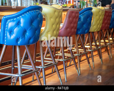 Blu, giallo e rosso cuoio Sedie per bar allineati nella parte anteriore del banco bar Foto Stock