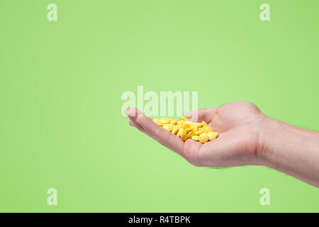 Pillole di giallo in mano su sfondo verde. Foto Stock