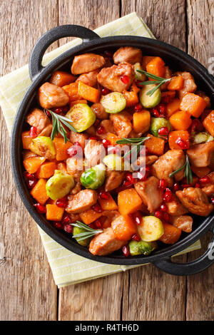 Delizioso pollo cucinato con verdure e rosmarino in salsa di melograno close-up in una padella sul tavolo. Verticale in alto vista da sopra Foto Stock