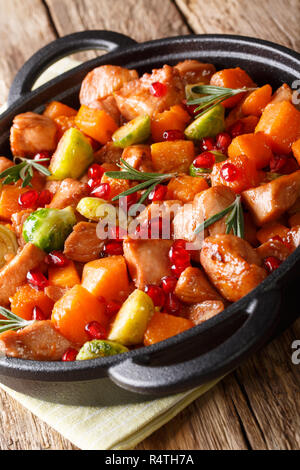 Spezzatino di pollo con patate dolci, i cavoli di Bruxelles in salsa di melograno close-up in una padella sulla tavola verticale. Foto Stock