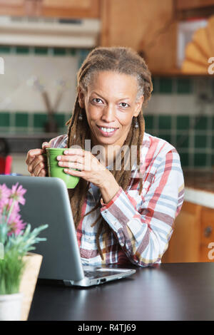 Bella donna azienda tazza da caffè accanto al laptop Foto Stock