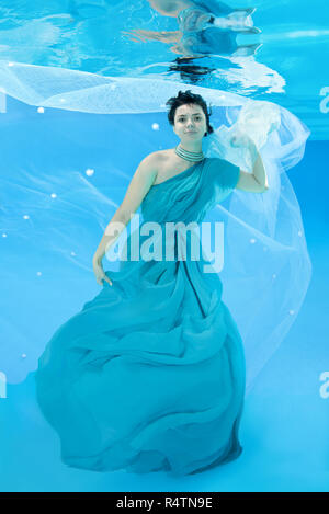 Giovane donna in lungo, vestito blu pone sotto l'acqua Foto Stock