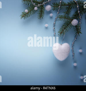 Composizione naturale con rami di abete bianco a forma di cuore decorazione di Natale, bianco snowballs artificiale e argento catena colorata su carta blu. Squ Foto Stock