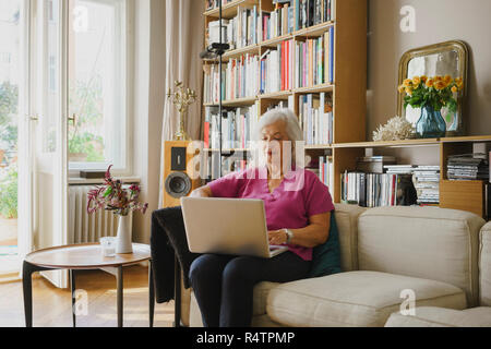Senior donna utilizzando computer portatile sul divano Foto Stock