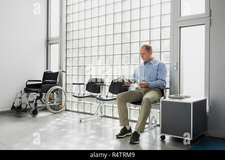 Paziente di sesso maschile in attesa, rivista di lettura in clinica in sala d'attesa Foto Stock