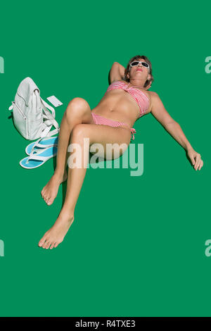 Donna in bikini a prendere il sole su sfondo verde Foto Stock