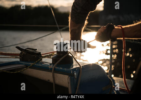 Silhouette di marinai mani su una fune del verricello a bordo di una barca a vela al tramonto. Girato con una messa a fuoco selettiva. Foto Stock