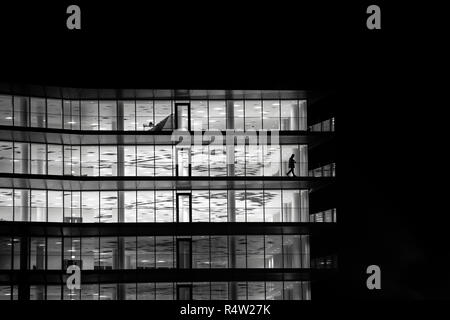 Una solitaria figura passeggiate lungo il balcone di un vuoto di edificio per uffici di notte a Bristol nel Regno Unito. Foto Stock