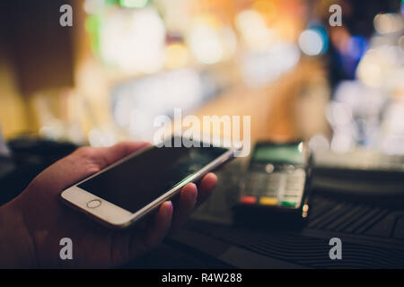 Primo piano di un cliente utilizzando la sua carta di credito e la tecnologia nfs per pagare un barista per il suo acquisto presso una caffetteria. Foto Stock