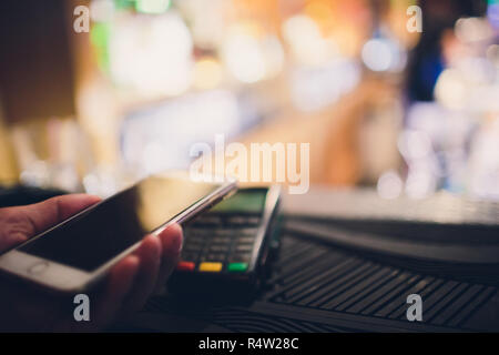 Primo piano di un cliente utilizzando la sua carta di credito e la tecnologia nfs per pagare un barista per il suo acquisto presso una caffetteria. Foto Stock