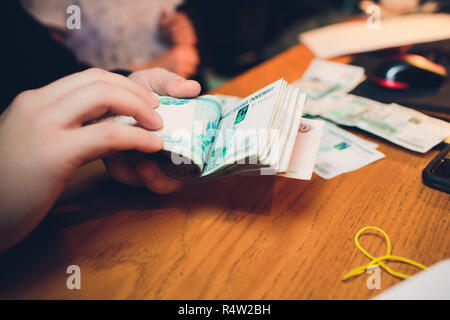 Maschio di mano trattiene una pila spessa di denaro contante. Milioni di rubli russi. Il concetto di un ricco patrimonio, profitti, business e finanza. Cinque millesimo fatture banconote. A lotti mazzette di denaro. Foto Stock