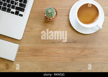 Scrivania in legno tavolo con computer laptop, disco rigido esterno, cactus e tazza di caffè. Vista da sopra con copia spazio. Foto Stock