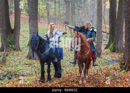 2 (due) pericolosi scandinavian viking guerrieri a cavallo e assi di sollevamento sopra la testa nella foresta, pronti per la battaglia. Northern guerrieri vichinghi ready t Foto Stock