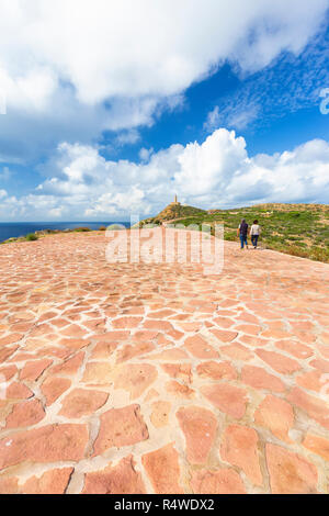 Due persone passeggiate a Capo Sandalo con il faro in background. Isola di San Pietro, Sud Sardegna provincia, Sardegna, Italia, Europa. Foto Stock