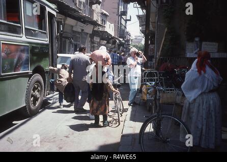 Scena di una strada stretta riempito con pedoni e traffico veicolare, in Damasco, Siria, Giugno 1994. Al centro della cornice di un turista occidentale fotografie di stallo del mercato dal lato della strada. A bordo sinistro di un giovane ragazzo si arrampica su di un autobus di città dotate di pubblicità in arabo per i vari sapori della marca di schiacciamento di soda. () Foto Stock