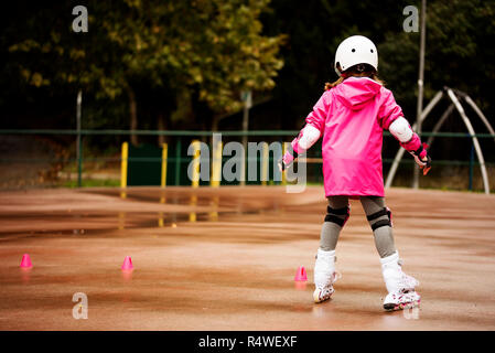 Una piccola ragazza caucasica rullo principiante in autunno nel parco la giornata piovosa. Foto Stock