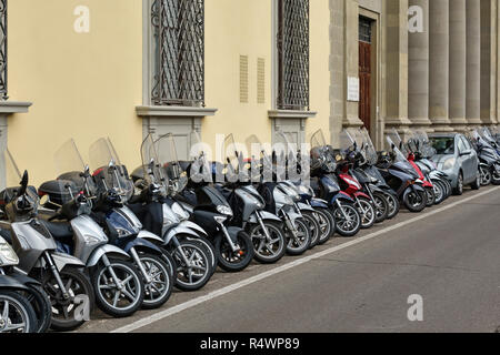 Firenze, Toscana, Italia. Una lunga fila di ordinatamente parcheggiata motociclette e ciclomotori e scooter, con una piccola macchina schiacciata in Foto Stock