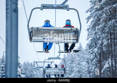 Persone con sollevamento di sci su ski-lift in montagna su terreni innevati giorno Foto Stock