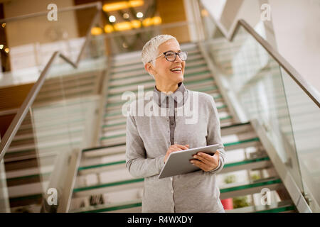 Piuttosto, positivo, invecchiato donna con sorriso raggiante tenendo compressa in un ufficio moderno Foto Stock