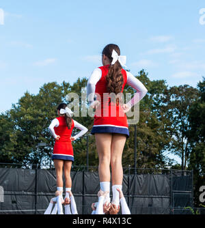 Due squadre di high school cheerleaders tenendo il loro compagno di squadra dai loro caviglie durante una routine. Foto Stock