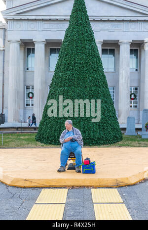 LINCOLNTON, NC, Stati Uniti d'America-11/25/18: Uomo sovrappeso con fotocamera si siede di fronte non decorato ad albero di Natale, in attesa per la parata. Foto Stock