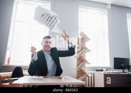 Un bel uomo seduto in ufficio e gettando papers in aria Foto Stock