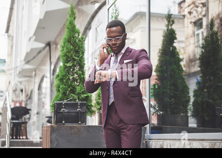 Ritratto di un giovane e bello African American businessman parlando in un vestito per telefono. Preparazione per una riunione di affari. Foto Stock