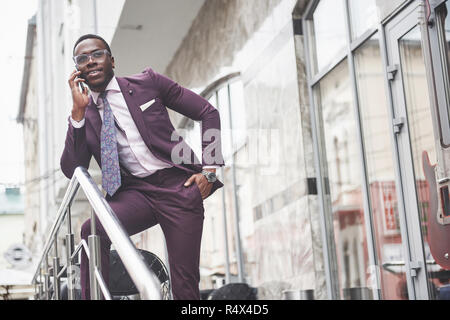 Ritratto di un giovane e bello African American businessman parlando in un vestito per telefono. Preparazione per una riunione di affari. Foto Stock