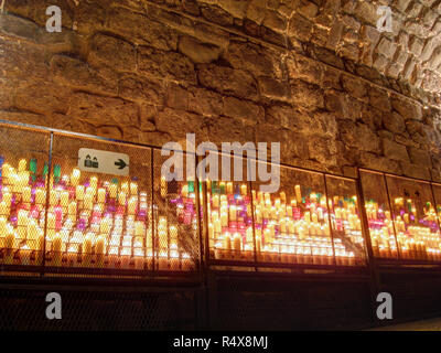 Un gruppo di colorate candele votive accese per la devozione in un antico in pietra cripta di santa nel monastero di Santa Maria di Monserrat, Catalogna, Spagna Foto Stock