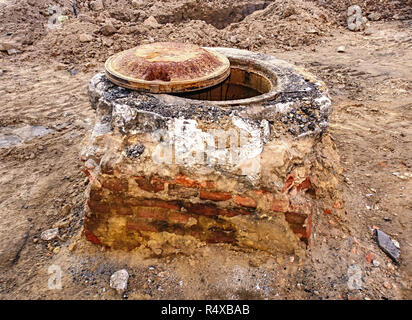 La ricostruzione della strada, tombino rotto con coperchio in acciaio. Tombino con metallo arrugginito coperchio in asfalto screpolato superficie Foto Stock