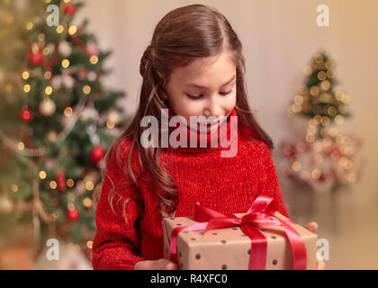 Grazioso fanciullo ragazza con la presente confezione regalo vicino albero di Natale a casa. Foto Stock