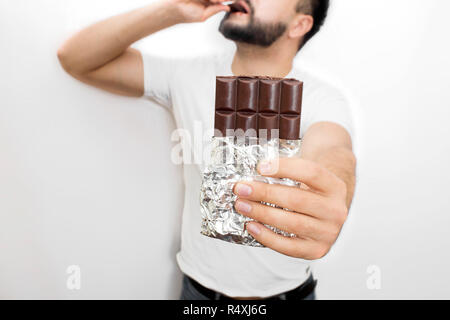 Tagliare vuew barra di cioccolato in giovane mano d'uomo. Egli tiene. Anche guy mette pezzo di cioccolato in bocca con anothe mano. È deliziosa. Isolato su sfondo bianco. Foto Stock