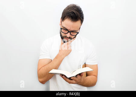 Considerato giovane uomo in bicchieri permanente e la lettura del libro. Egli tiene nella mano sinistra. Un altro in sotto il mento. Isolato su sfondo bianco. Foto Stock