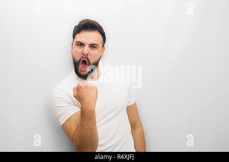 Stupendo e persona felice sorge e pone sulla fotocamera. Egli tiene in mano il pugno e avere la gioia. Egli è eccitato. Isolato su sfondo bianco. Foto Stock