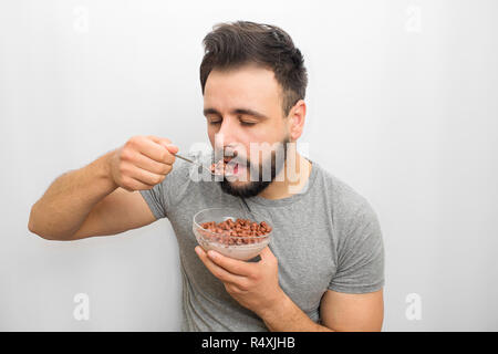 Bella bruna si erge e mangia cioccolato chip rotondo con il latte. Egli sta per mettere il cucchiaio con esso in bocca. Guy è sonnolenta. Egli guarda verso il basso. Isolato su sfondo bianco. Foto Stock