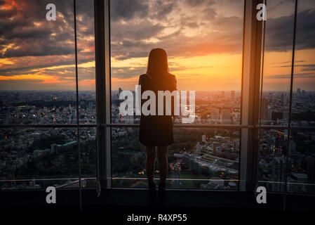 Vista posteriore della donna di viaggiatori che cercano lo skyline di Tokyo e vista dei grattacieli sul ponte di osservazione al tramonto in Giappone. Foto Stock