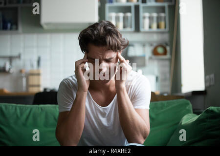 Giovane uomo seduto sul divano di casa hanno un mal di testa Foto Stock