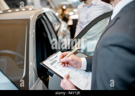 Manager il riempimento autonoleggio documenti in piedi nello showroom con auto sullo sfondo Foto Stock