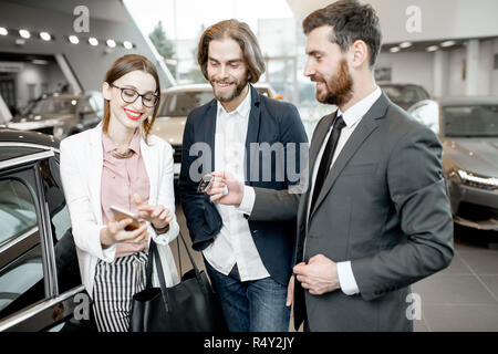 Addetto alle vendite dando chiavi da una nuova vettura per un happy business giovane in piedi insieme nella showroom delle auto Foto Stock