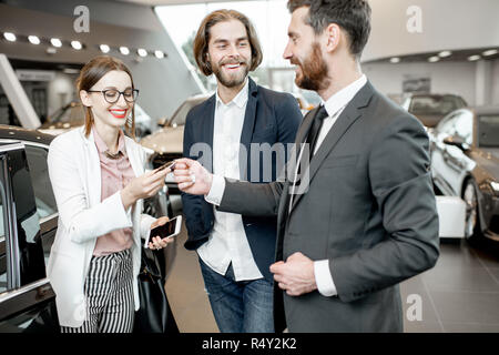 Addetto alle vendite dando chiavi da una nuova vettura per un happy business giovane in piedi insieme nella showroom delle auto Foto Stock