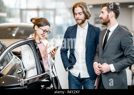 Addetto alle vendite in piedi con la giovane azienda giovane vicino alla vettura di lusso nello showroom Foto Stock