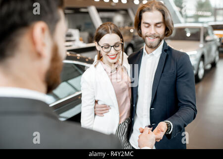 Addetto alle vendite dando chiavi da una nuova vettura per una bella azienda giovane in piedi insieme nella showroom delle auto Foto Stock